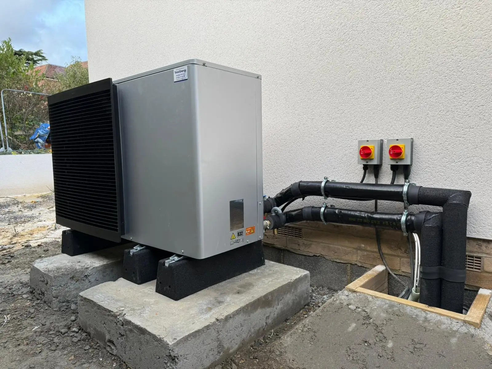 Air-source heat pump on an external plinth with electrical isolators, wired on a new build in Poole