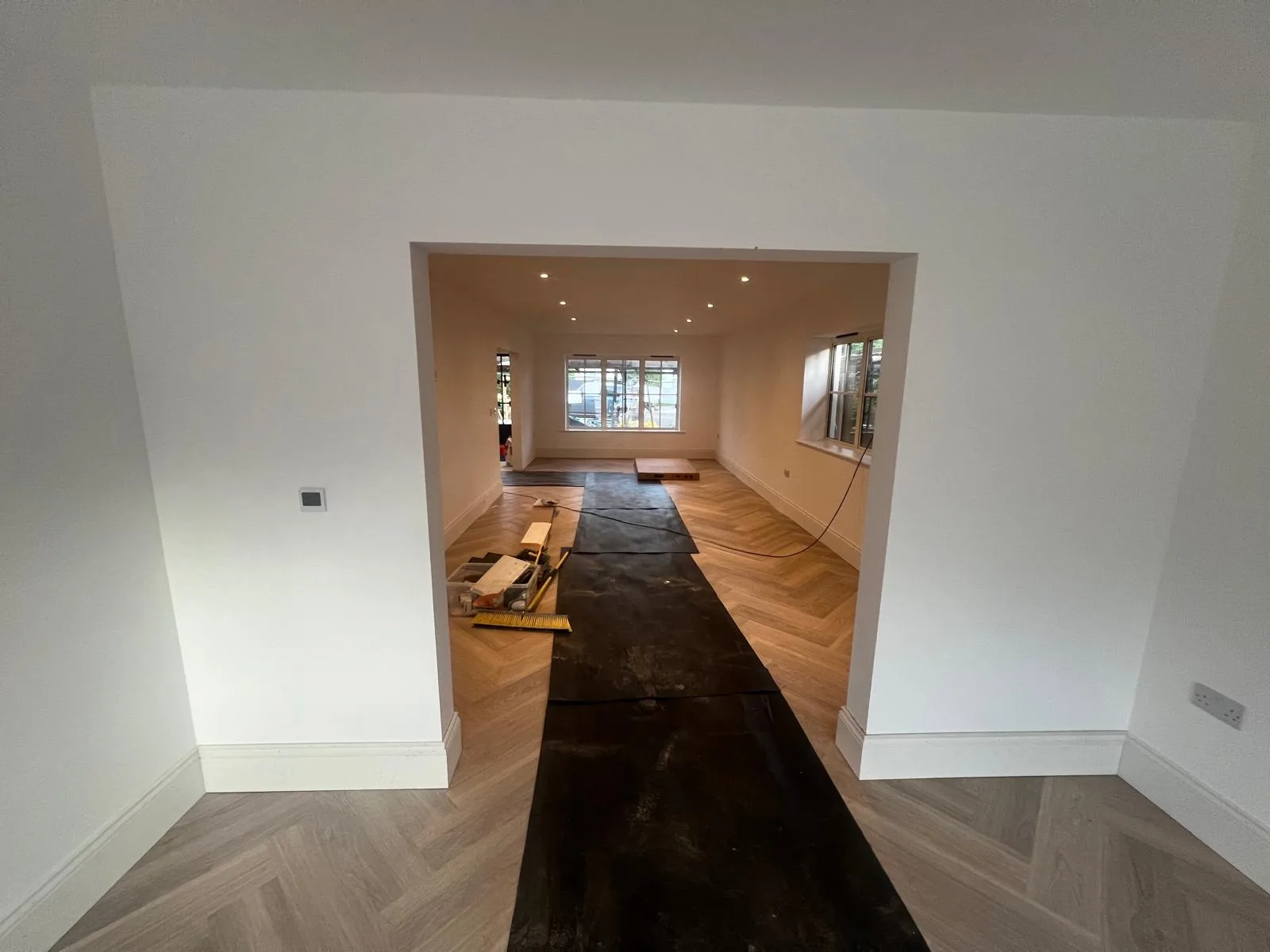 Open-plan living space with recessed downlights and herringbone flooring in a self-build home in Poole